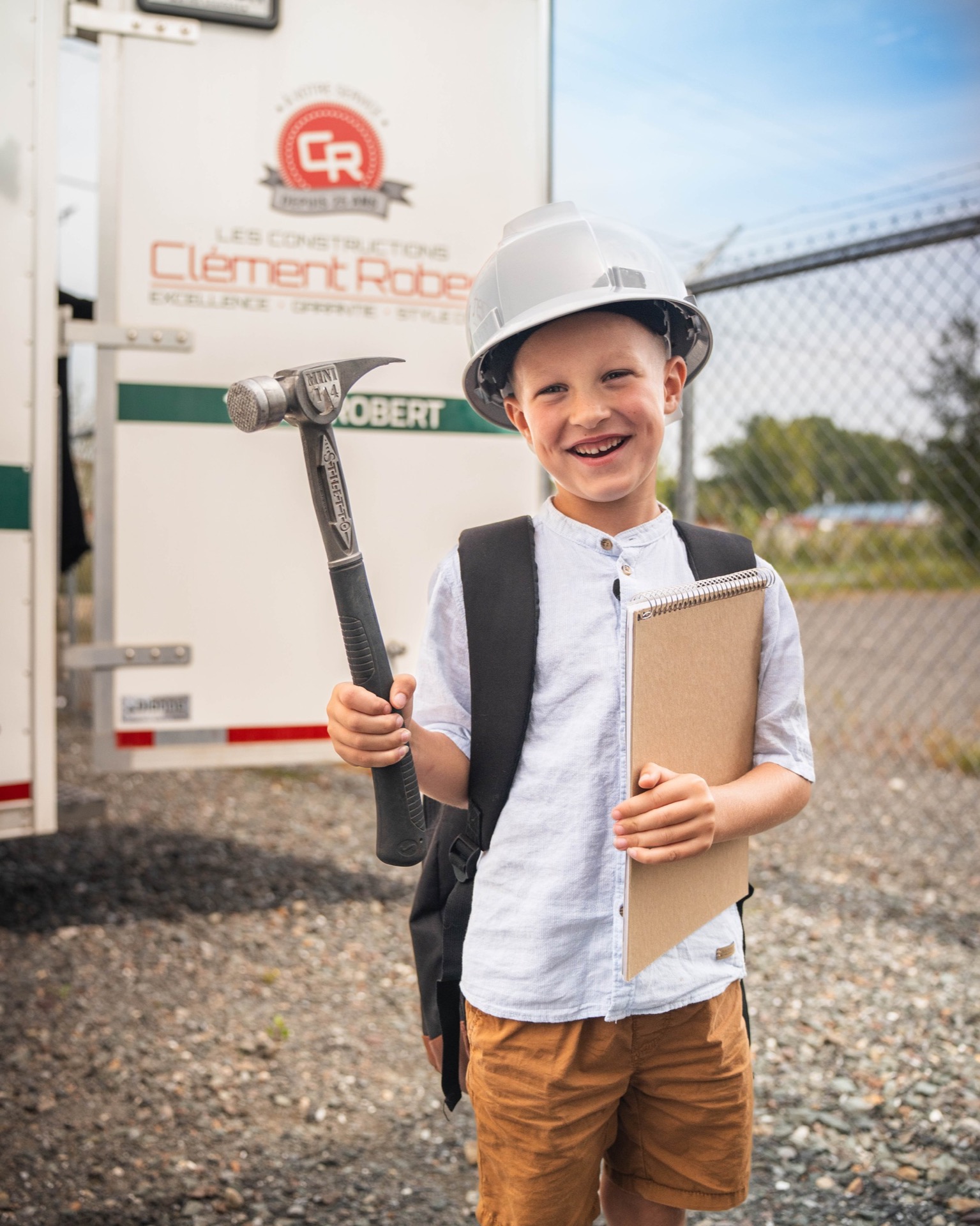 Jeune enfant en casque de chantier, devant la remorque Clément Robert